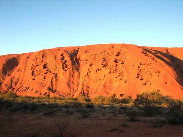 ... Wind und Sand schmirgelten Gesichter in die Flanken des Uluru ...