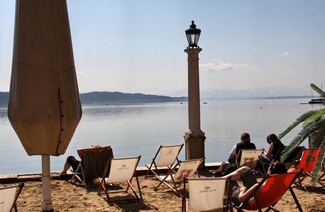 Sandstrand und Liegestühle mit Blick auf die Alpen