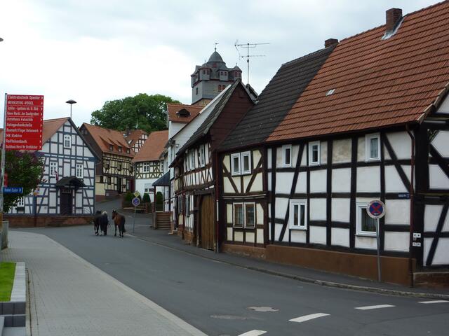 Dorfstraße heute; Perspektive zur Rathausstraße und zum Steinweg mit Wehrkirche wie im vorherigen Bild. Mit Pferden, die zu ZICKs Hof geführt werden.