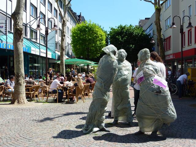 Die "Drei SCHWÄTZER" - verpackt nach CHRISTO - auf dem Seltersweg und andere Gießener interessierten sich bei schönem Wetter nicht für die FDP-Europawahlkampf-Veranstaltung auf dem Kirchenplatz.