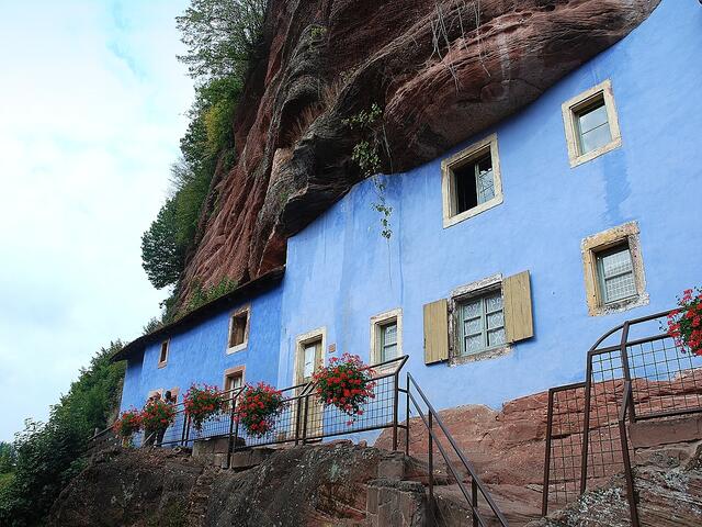 Graufthal - blaue Hauswände inmitten roter Sandsteinfelsen. Im Mittelalter sollen die Felsdächer bereits von den Benediktinerinnen zur Lagerung ihres Brennholzes und ihrer Lebensmittel benutzt worden sein.