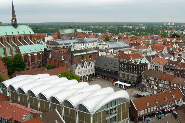 Am Markt im Vordergrund liegende, versetzt angeordnete Weinflaschen als Dachform, mit scheinbar durchgehender Oberflächenverkleidung aus Aluminium (Fertigstellung des Textilhauses 2005), gegenüber die Schaufassaden des Rathauses