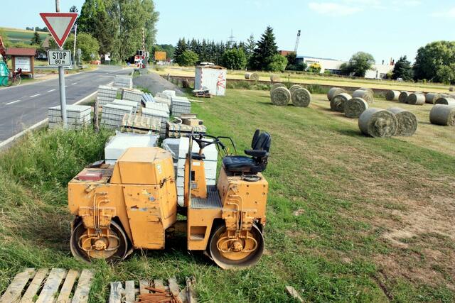 Baumaterialien neben der Straße. Der Bahnsteig ist links vom Bahnübergang. (26.06.2010)