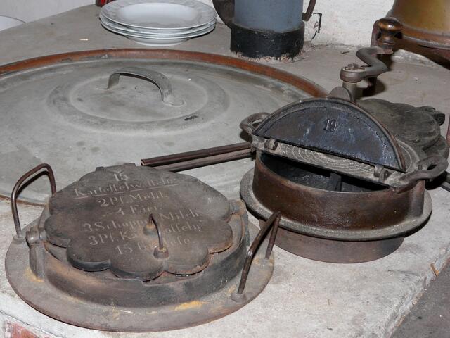 Wofür wurde das Gerät rechts im Bild verwendet? Auf dem Waffeleisen kann man ein Rezept für Kartoffelwaffeln lesen.