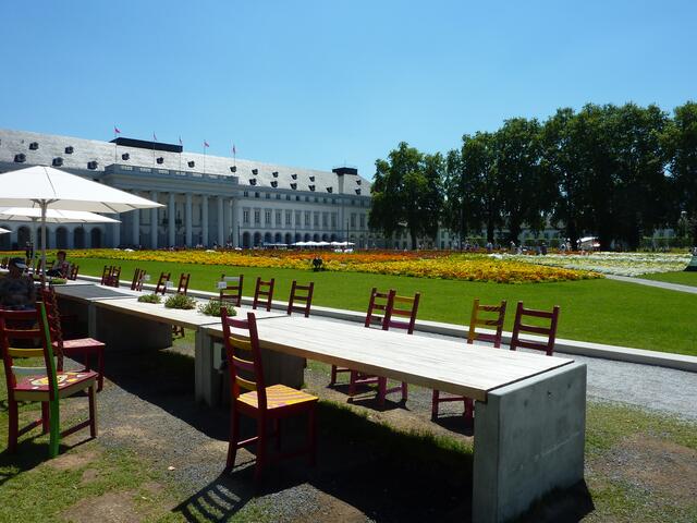 Eine lange Tafel mit bunt bemalten Stühlen lädt zum Ausruhen ein. In jeden zweiten Tisch sind Pflanzwannen eingelassen.