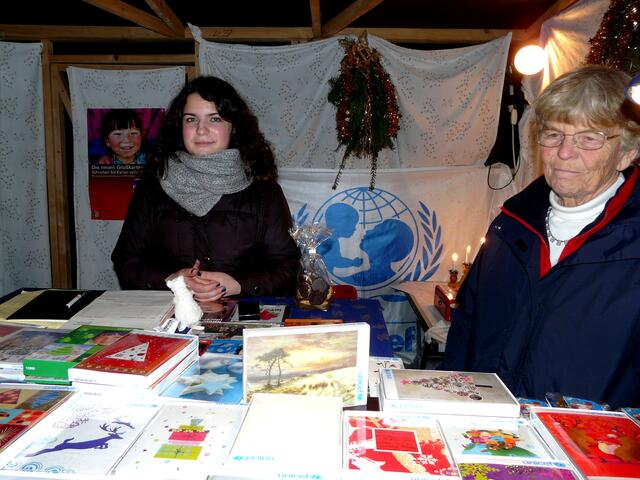 UNICEF-Grußkarten - Ehrenamtlicher Einsatz auf dem Weihnachtsmarkt. Die Enkelin begleitet ihre Großmutter an diesem Tag.