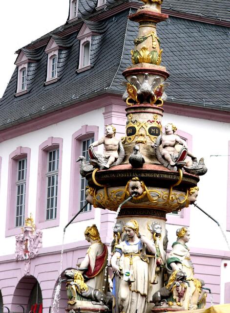 In welcher Stadt steht dieser Brunnen. Wie heißt er? Die Figuren - um den Brunnenstock- präsentieren die vier Tugenden: Weisheit, Gerechtigkeit, Tapferkeit, und Mäßigkeit. - Der Petrusbrunnen  auf dem Hauptmarkt in Trier.