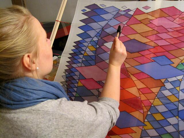Letzte Farbtupfer werden auf das Seidentuch gemalt.