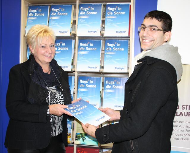 Reise-Expertin Monika Wackermann übergibt den Reisekatalog "flugs in die Sonne" an einen Kunden.