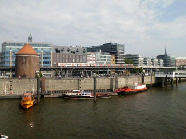 Blick vom Schiff aus an Land zwischen Baumwall und Landungsbrücken