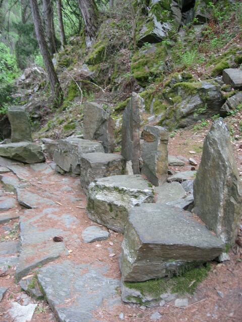 Die Steinsitze im angedeuteten Gerichtshof. Das Gelände ist steil, der Hintergrund felsig, wild zerklüftet, bedrohlich. Es spricht für sich selbst.