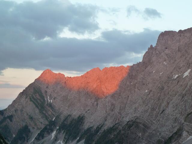 Die Sonne geht unter und verwandelt die Bergspitze in ein glühendes Rot