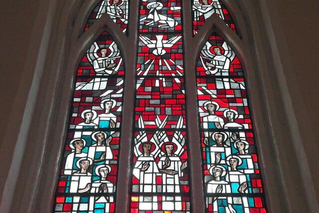 Im oberen Teil des mittleren Fensters ist eine Taube als Symbol des Heiligen Geistes abgebildet, umgeben von musizierende Engeln und den zwölf Aposteln.