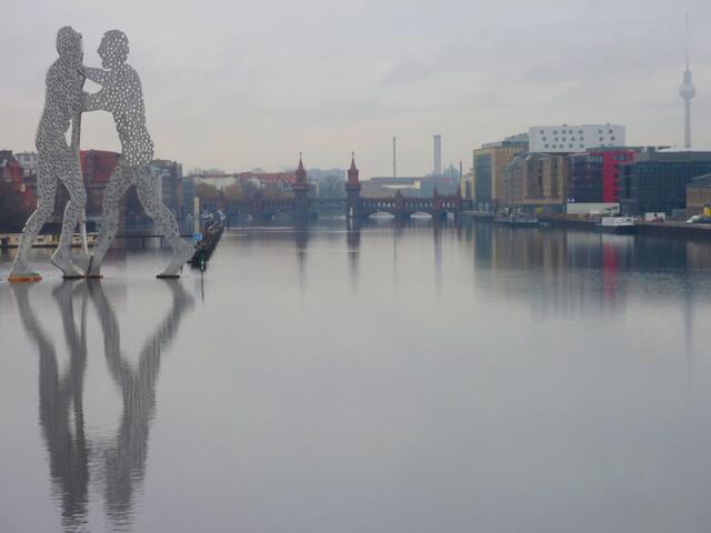Die Figuren sollen die Verbindung zwischen Ost und West verkörpern. In der Mitte ist die Oberbaumbrücke und ganz rechts ist der Fernsehturm am Alexanderplatz zu sehen.