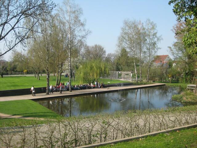 Blick von oben auf den Schlossweiher mit Springbrunnen, an dem sich frühzeitig Besucher einen Sitz-Platz sicherten
