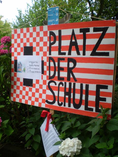 Plakat PLATZ DER SCHULE mit BAKI-STIMMZETTEL für Frau Bundeskanzlerin Dr. Angela Merkel, darüber die Symbole für LIEBE, FRIEDEN und MENSCHENRECHTE , darunter: "Bremer Erklärung vom 8. Mai 2013" und das Märchen "Die Bremer Stadtmusikanten und die Friedenstaube"