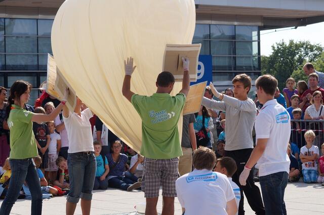 Der Ballon pendelt im Wind hin und her. Damit er hierdurch nicht beschädigt wird stützen ihn Helfer mit Pappschilden.