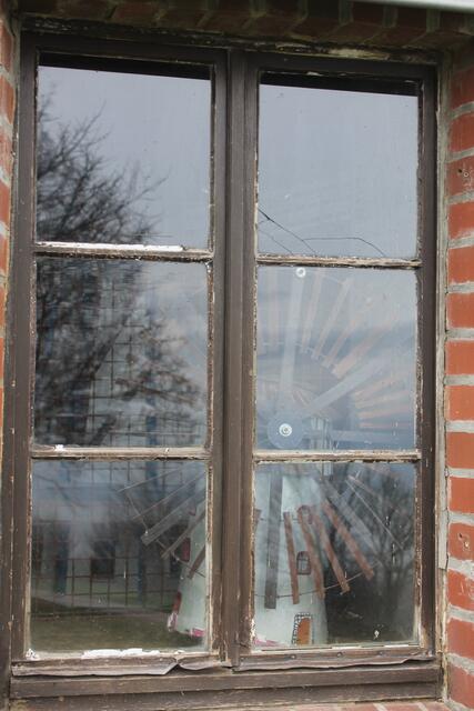 Eine Mühle im Kleinformat ist hinter einem Fenster zu sehen. Leider blendet es zu sehr.