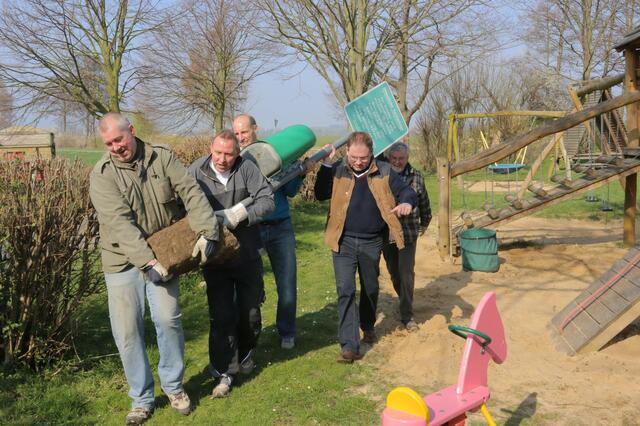 Harm Kolberg, ein Helfer, Martin Sondermann, Christoph Meinke und ein weiterer freiwilliger Helfer tragen gemeinsam Papierkorb und Spielplatzschild zum neuen Standort.
