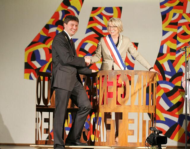 beide Bürgermeister vor dem Geschenk aus Meitingen einer Bank aus Corten-Stahl