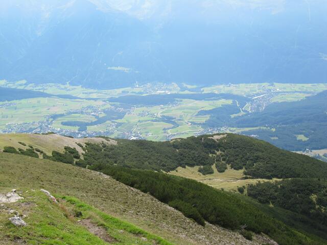 Blick vom Gipfel ins Tal auf den Ort Stams. In der Mitte vor den Bergen sind zwei kleine senkrechte Striche, die Skischanzen. Gleich rechts daneben das Kloster Stams.