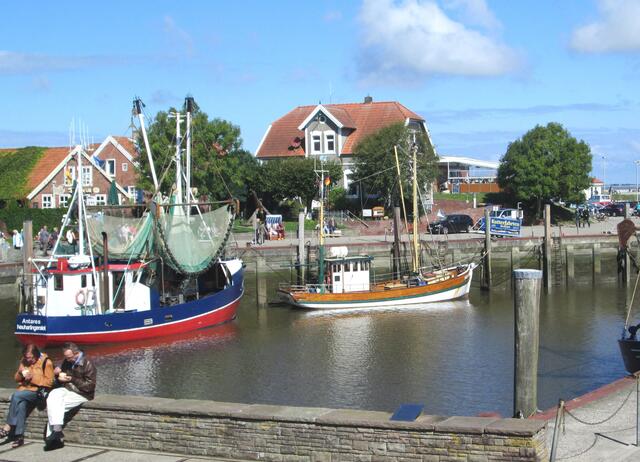 Eisessen an der Hafenmauer in Neuharlingersiel. Im Hintergrund das Boot Antares, benannt nach dem hellsten Stern im Skorpion, der eine ähnliche Helligkeit wie der Mars hat.
