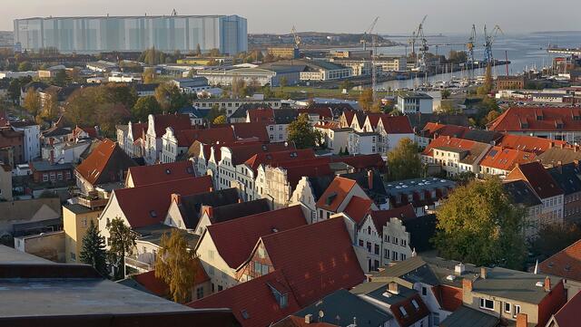 Hinter der Altstadt das Werftgelände: Die 1998 errichtete Dockhalle ist 395 m lang, 155 m breit und 76 m hoch. In ihr werden derzeit Produkte für Offshore-Anlagen hergestellt. Im Vordergrund die Lübsche Straße (diagonal) mit den prächtigen Giebelhäusern. Foto: Helmut Kuzina