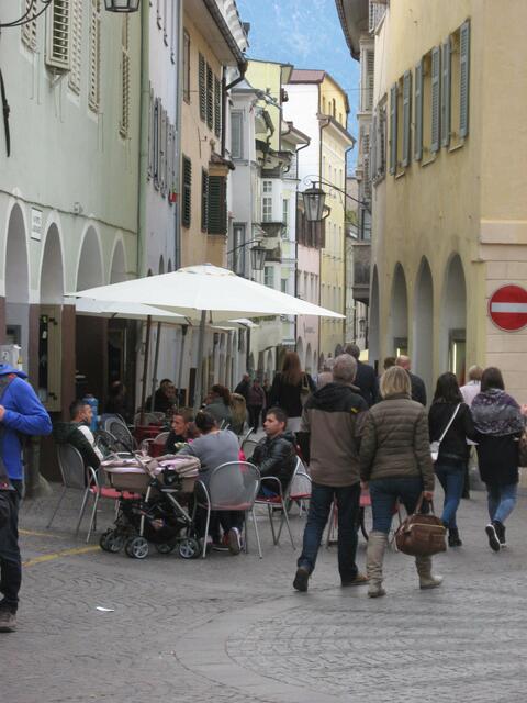 Reges Leben in den Laubengassen von Meran. Wir fügen uns nahtlos ein ins Treiben. Mich locken wie so oft, nicht die vielen Schmuck u. Modegeschäfte, sondern Speck- u. Wurstläden. Schinkenstücke im Ganzen hängen aufgereiht, prall und saftig, im Schaufenster. Ab sofort knurrt der Magen. Dann noch vorbei an mehreren Panivicio-Läden, und ich brauche ganz schnell "ein bisschen" Geld zum Einkaufen.