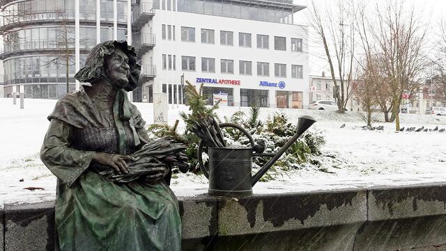 Trotz der Schneeschauer sitzt die Blumenfrau Bertha Klingberg (die Bronzeskulptur von Bernd Streiter aus dem Jahr 2010 erinnert an Schwerins Ehrenbürgerin) „unverdrossen“ am Ufer des Burgsees. Foto: Helmut Kuzina
