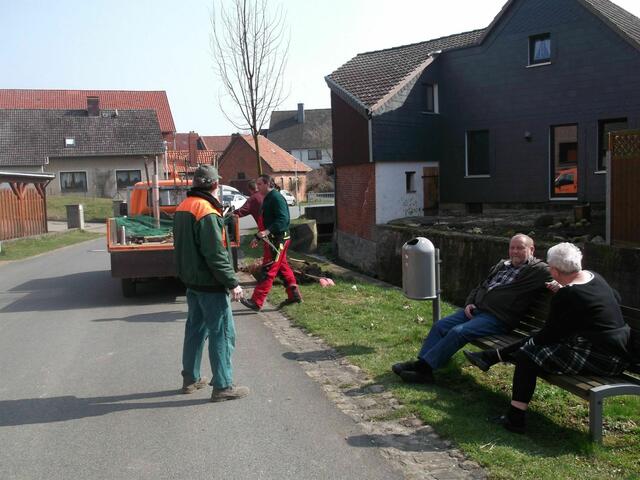 2. Ortsbürgermeister (stehend) und Anwohner (sitzend) sind beim Aufstellen der Linde anwesend.
