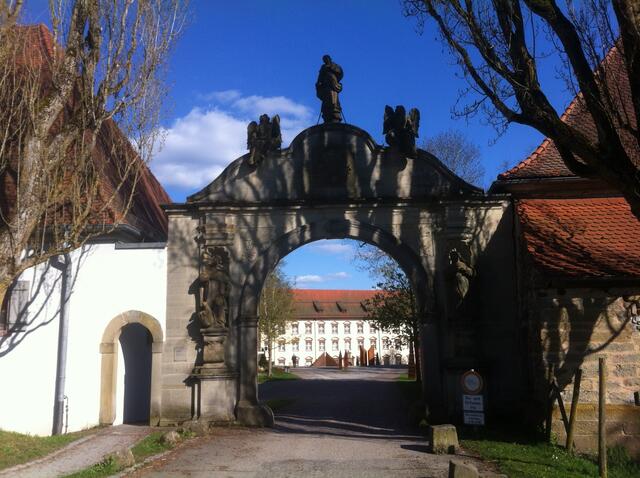Durch das Tor erscheint im Hintergrund des erstaunlich große, schlossähnliche Konventgebäude.