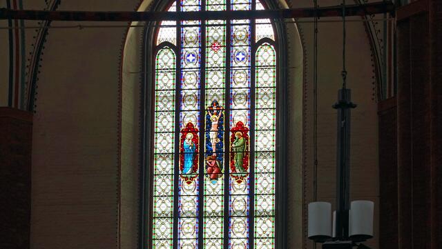 Über dem Hauptaltar zeigt das mittlere Ostfenster eine Glasmalerei aus der Zeit um 1840. Dargestellt sind der gekreuzigte Jesus, links seine Mutter Maria, rechts der Apostel Johannes, unter dem Kreuz kniet Maria Magdalena. Foto: Helmut Kuzina