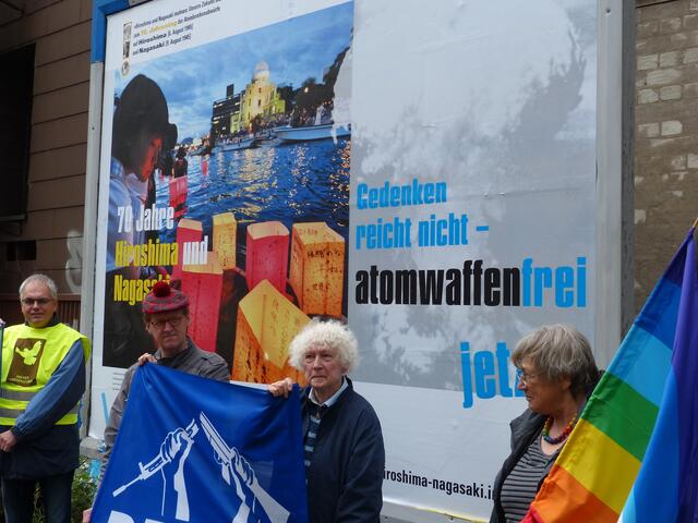 Auf der Plakatwand ist zu lesen: „Gedenken reicht nicht – atomwaffenfrei jetzt!“ Zu sehen ist ein japanisches Mädchen an der Gedenkstätte in Hiroshima.