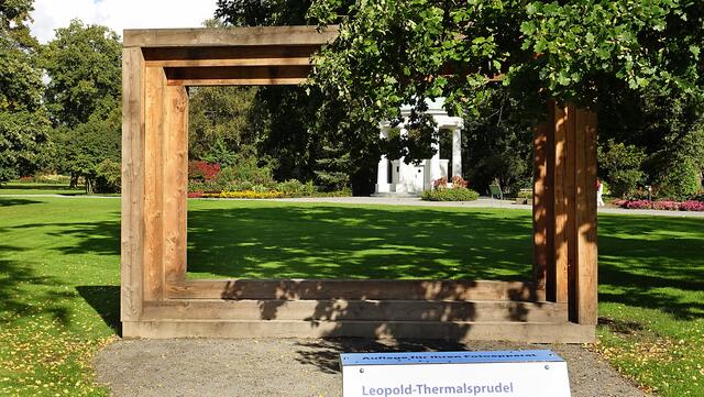 Neuerdings steht ein Landschaftsrahmen im Kurpark; Besucher können ihren Fotoapparat auf der Stütze (im Vordergrund) ablegen, sich in den Rahmen stellen und sich so per Selbstauslöser zusammen mit dem Leopold-Thermalsprudel aufnehmen. Foto: Helmut Kuzina