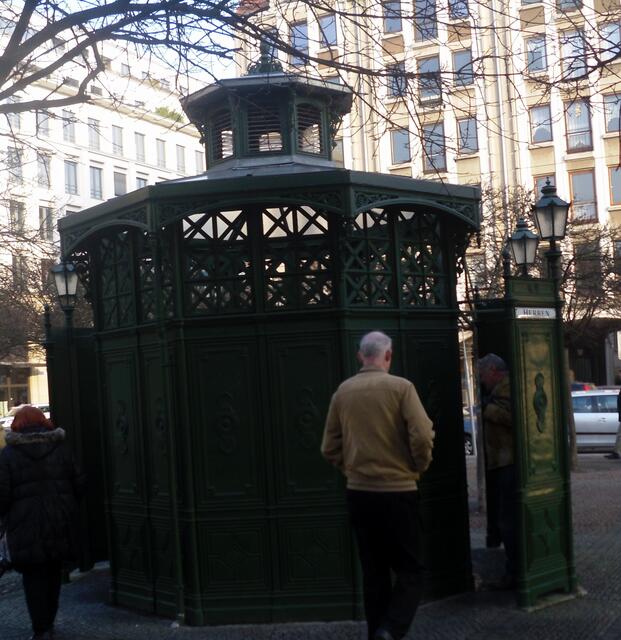 “Café Achteck”, scherzhafte Bezeichnung für die aus grünlackiertem Metall gefertigten und heute im Stadtgebiet kaum noch zu findenden Pissoirs für Herren, wie sie in Berlin um 1900 typisch waren.