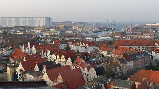 Im Vordergrund läuft die Lübsche Straße mit den Giebelhäusern schräg durch das Bild; im Hintergrund sind die Werfthalle (links), der Westhafen und die Wismarbucht zu erkennen. Foto: Helmut Kuzina