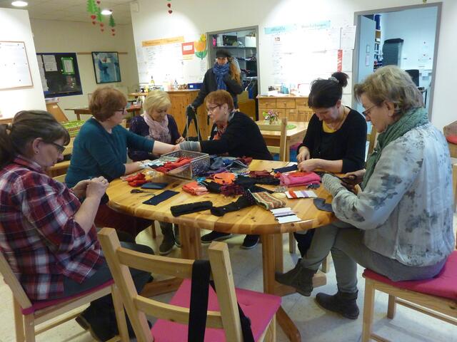 Gerlinde berät gerade Tina. Der Stoff wird Arm und Hand angepasst. Gabi, Moni, Christine (Leiterin des MGH) und Ingrid sind gerade konzentriert bei der Arbeit. Im Hintergrund schaut Silvi zu.