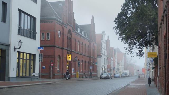 Der Nebel hat seinen eigenen Ausdruck, er dämpft die Geräusche, begrenzt den sichtbaren Raum der Mecklenburger Straße, an der das Hauptpostgebäude steht. Foto: Helmut Kuzina
