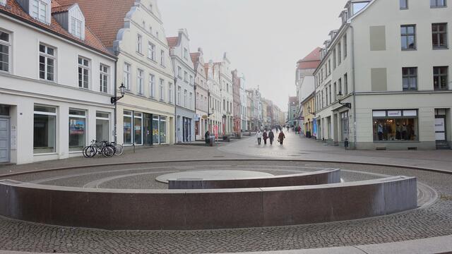 Auf beiden Seiten zeigt die Krämerstraße mit ihren vielen Geschäften und Restaurants farbige Hausfassaden - wenn es nicht so trüb und neblig wäre, könnte man sie besser erkennen; im Vordergrund die moderne Brunnenanlage (die die Sicht auf die Giebelhäuser nicht verdecken soll). Foto: Helmut Kuzina