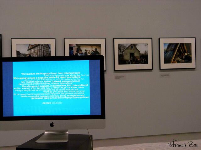 Bildschirmpräsentation, dahinter einige Fotos der Ausstellung