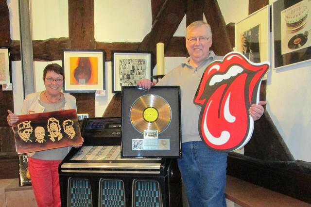 Elisabeth Skupin, die Museumsbeauftragte der Stadt Battenberg, und der Sammler Günter Wack präsentieren von links einen Holzschnitt der Stones (von einem französischen Künstler), die Musikbox mit etwa 80 Singles von den Rolling Stones, eine goldene Schallplatte (die einst Keith Richards für Exile On Main Street erhielt) und das Bandlogo „Tongue and Lips“.