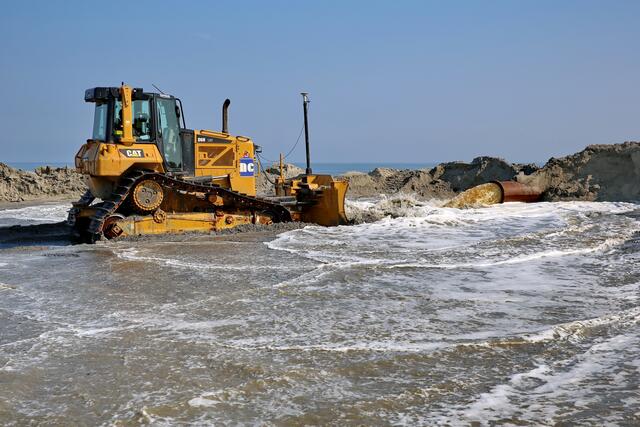 Hier schiebt die Raupe gerade die Senke wieder zu, die der starke Wasserstrahl in den Sand gebohrt hat.