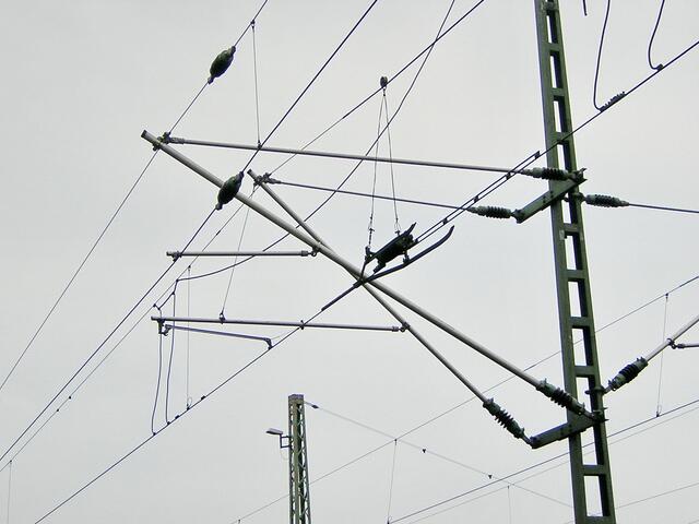 Große Isolatoren halten den Strom von den Masten fern. Aber sie sind direkt am Mast montiert. Ihre Bauweise, die Rillen, herhindern einen Stromüberschlag oder dass Regen oder Eis eine Verbindung herstellen.