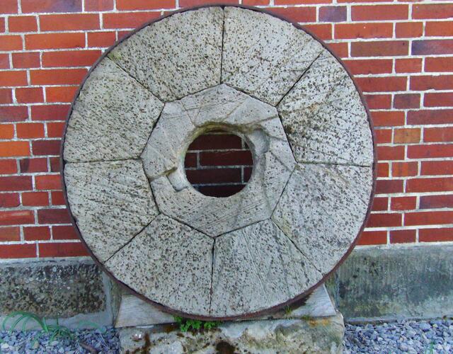 Neben einem Mahlstein erinnert ein Felsblock mit Inschrift an vergangene Zeiten.