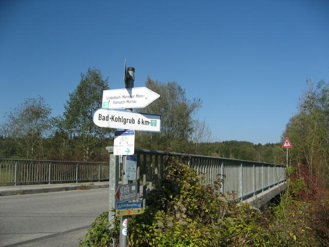 Ich überquere mit dem Rad die kleine Landstraße nach Grafenaschau und biege genau hier, vor der Brücke über den Lindenbach, rechts ab. Nun bin ich auf dem Natur-Radweg (aufgeschütteter Kiesweg) durchs Murnauer Moos, Richtung Murnau. (Teilabschnitt)