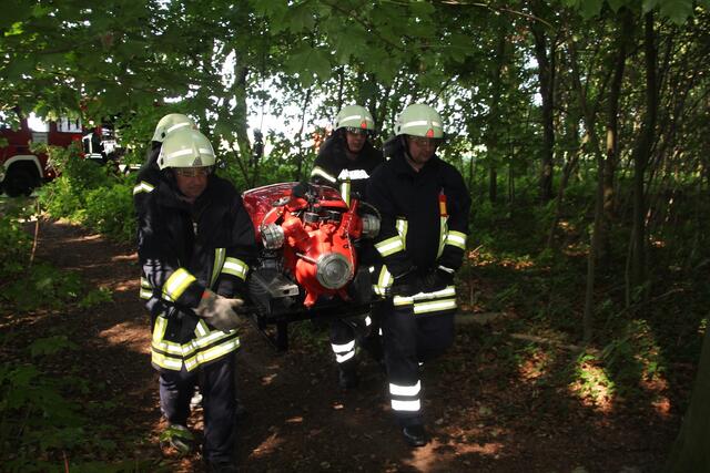 Über einen schmalen Pfad im Redener Wald wird eine Tragkraftspritze zur Wasserentnahmestelle getragen