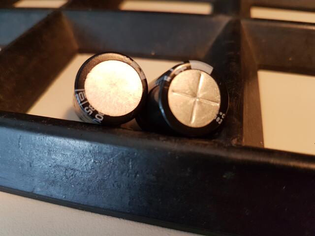 Zwei Kondensatoren. Links: Kondensator mit durchgehendem Boden aus Aluminium. Rechts: Kondensator mit angestanztem Alu-Boden, der nach einer vorbestimmten Laufzeit aufplatzt udd das Gerät somit funktions-unfähig macht. Mehr dazu auf dem nächsten Bild. Diese heimliche, absichtliche  Lebensdauerbegrenzung wird "Obsoleszenz eines Produkts" genannt.