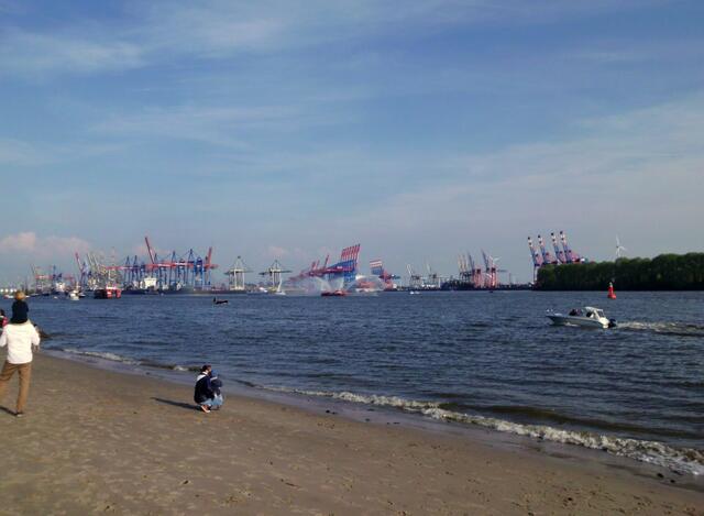 Der Auslaufparade voran das Feuerlöschboot mit seinen Fontänen - im Hindergrund die Kräne von Container-Terminals