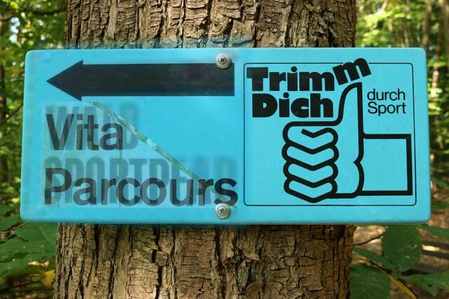 Wegweiser Vita-Parcours mit zwei darübergelegten Vorlagen zum Waldsportpfad