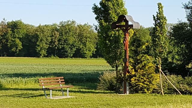 Gepflegte Ruhebank mit Kruzifix am Wegrand